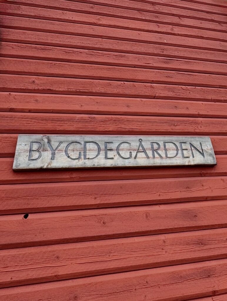 En bild på en träskylt mot faluröd fasad tillhörande Gopshus bygdegård. På skylten står det BYGDEGÅRDEN.